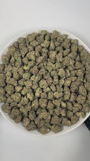 PUFFY Frosted Donut is an indica-dominant  hybrid THCa strain, expertly crafted from a potent cross between Girl Scout Cookies and Louis XIII. The aroma is a delightful blend of sweet berry, smooth vanilla, and fresh pine, creating a rich and inviting fragrance. Visually, the dense buds display bright green and deep purple hues, dotted with orange pistils and coated in sparkling trichomes. Consumers often report an initial euphoric and uplifting cerebral buzz that elevates mood, gradually transitioning into