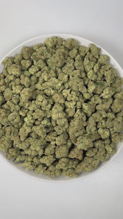 PUFFY Lemon Batter is an indica-dominant hybrid THCa strain, created from the fusion of Banana Punch GMO × Gorilla Diesel. The aroma is a sharp and zesty lemon, layered with pungent diesel notes and subtle chemical undertones, creating a bold, electrifying, and unmistakably intense scent profile. Visually, dense green buds with purple hues and fiery orange pistils are coated in sticky trichomes. Consumers often report that this strain provides a soothing, calming effect on the body while offering a balanced