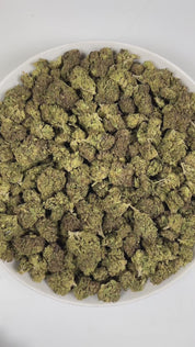 PUFFY Wedding Crasher is a balanced hybrid THCa strain, born from the flavorful union of Wedding Cake × Purple Punch. The aroma is a captivating blend of herbal, smoky, and gassy notes, creating a rich and distinctive scent profile. Visually, the buds are tightly formed, displaying green and purple hues highlighted by bright orange pistils and a thick coating of sparkling trichomes that create a frosty finish. Consumers often report feeling euphoric, focused, and deeply relaxed, accompanied by a happy, upli